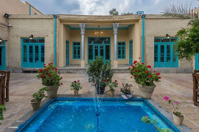 فواره حوض حیاط سرای هاتف میان گل‌های قرمز