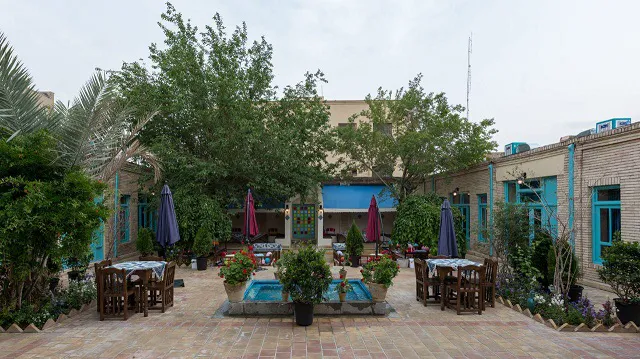 حیاط سرای هاتف با حوض، درختان و میزهای غذاخوری
