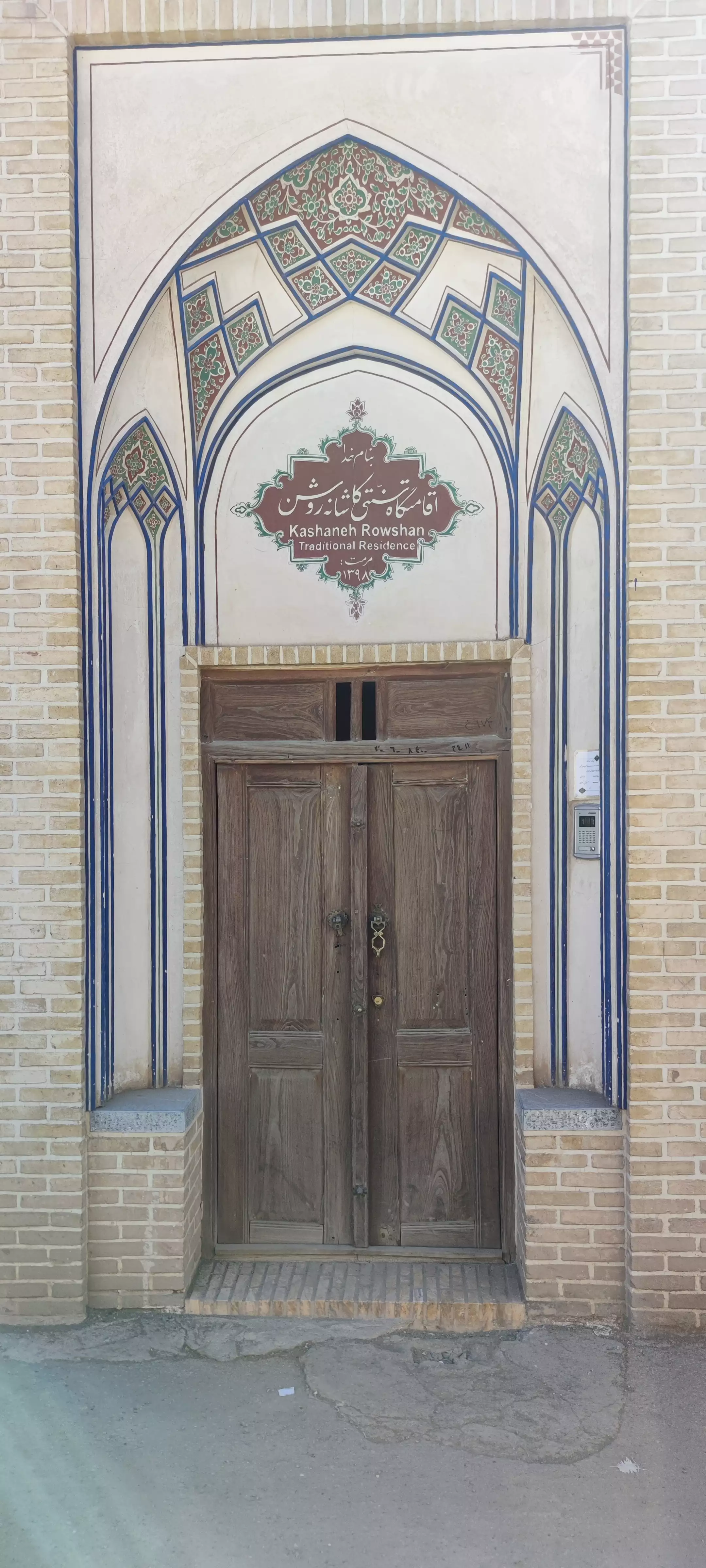در چوبی کاشانه روشن زیر طاق کاشی‌کاری‌شده