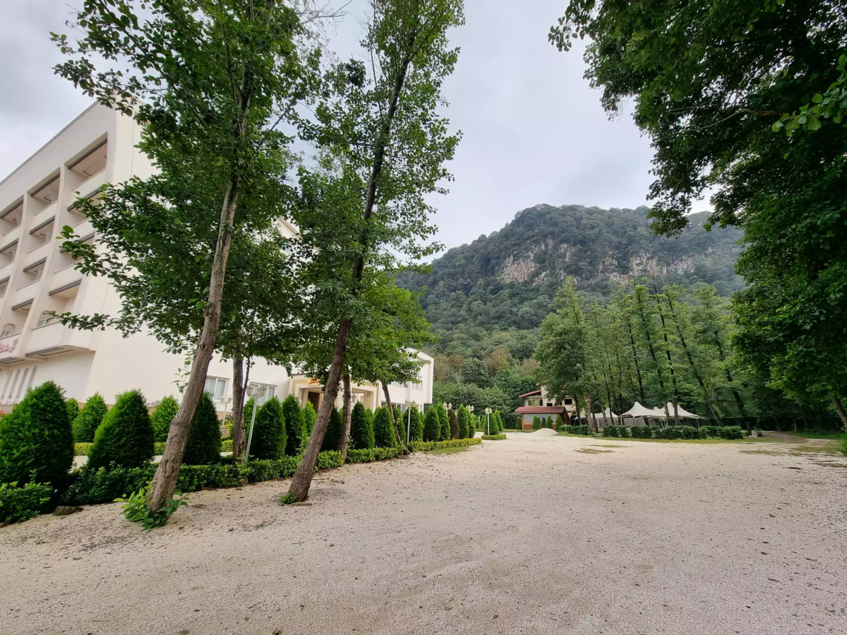 محوطه هتل شهرزاد با درختان و نمای کوهستان