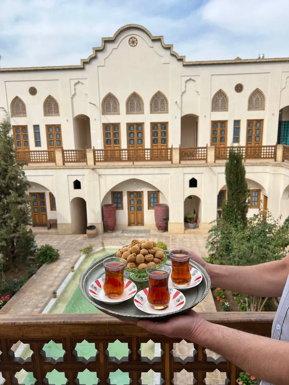 سینی چای در حیاط هتل ادیب با نمای بنای تاریخی