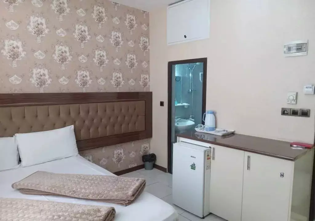 تخت اتاق هتل هرمس و یخچال کوچک