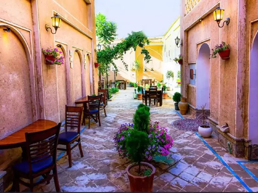 حیاط سنگفرششده هتل یاس با گلدان و میزهای چوبی